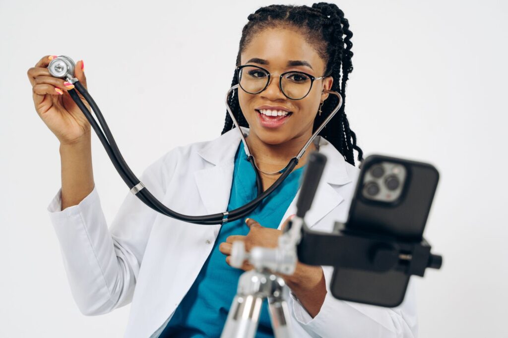 Médica sorridente gravando vídeo com o celular no consultório