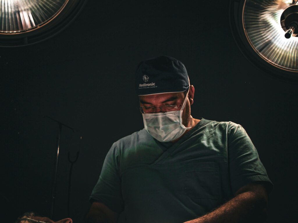 Cirurgião de máscara e touca em sala de cirurgia, luzes cirúrgicas ao fundo